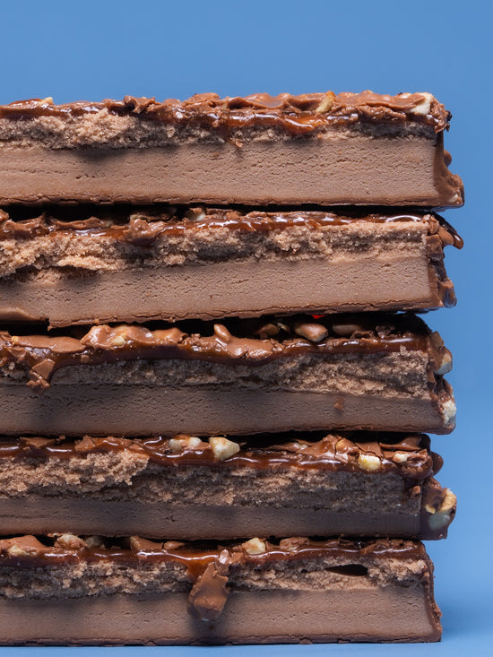 Stack of five Barebells Caramel Cashew protein bars showing cross-section with chocolate coating, caramel layer, and cashew pieces