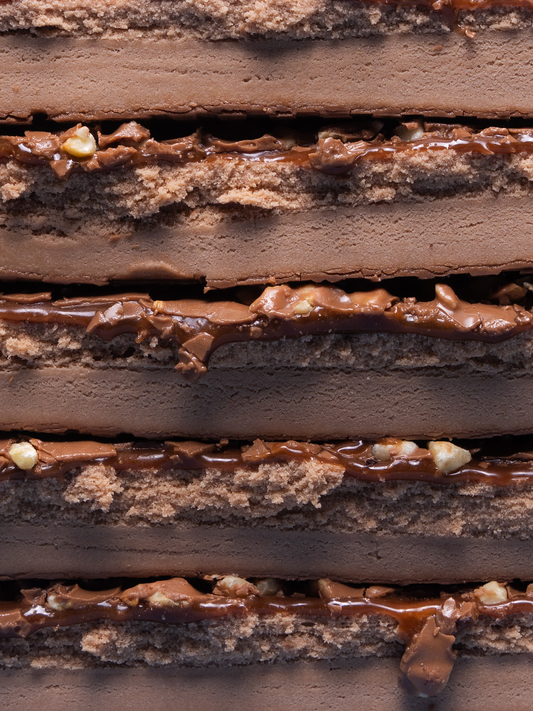 Barebells Caramel Cashew protein bar sliced to show layers of chocolate, caramel, and cashew pieces