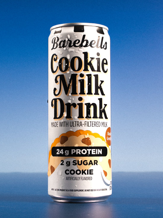 Barebells Cookie Milk Drink can with white and cream packaging featuring cookie graphics, 24g protein and 2g sugar on blue background