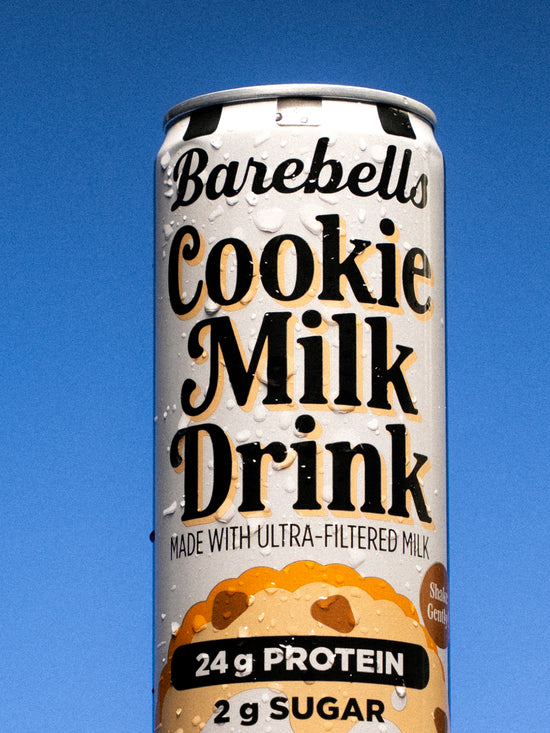 Barebells Cookie Milk Drink can with chocolate chip cookie imagery, 24g protein and 2g sugar labeled on packaging against blue background