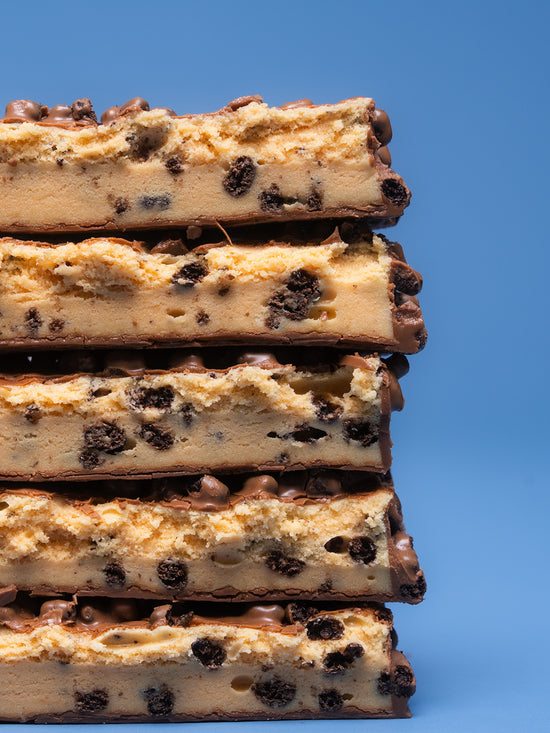 Stack of five Barebells Cookies and Cream protein bars showing cross-section with cookie pieces throughout tan filling and chocolate coating