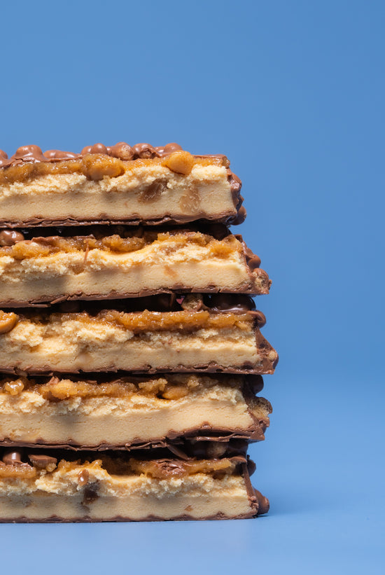 Stack of five Barebells Peanut Butter protein bars with chocolate coating and peanut pieces on blue background