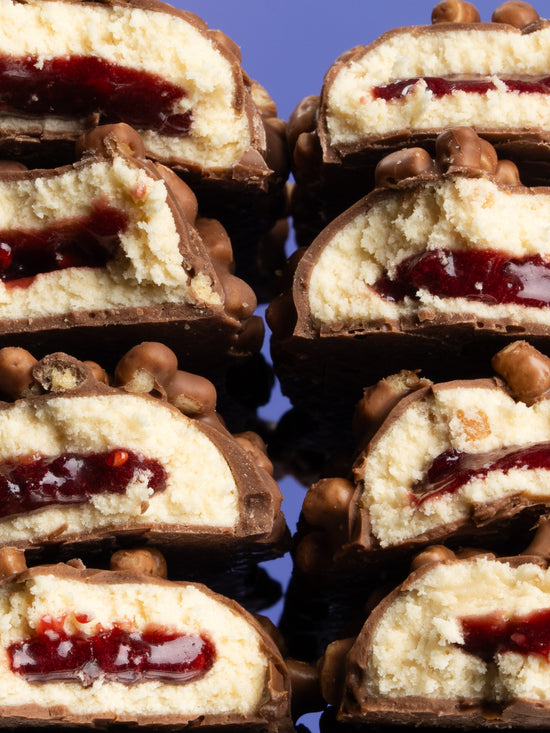 Cross-sections of Barebells Peanut Butter & Jelly bars stacked showing chocolate coating, cake layer, jelly center and peanut pieces