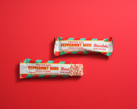 Two Barebells Peppermint Bark protein bars with white and turquoise packaging on red background, one wrapped and one showing the bar inside