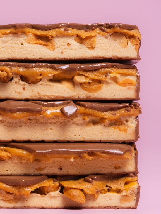 Stack of five Barebells Salted Peanut Caramel bars cut lengthwise showing layers of chocolate, peanut caramel and cake