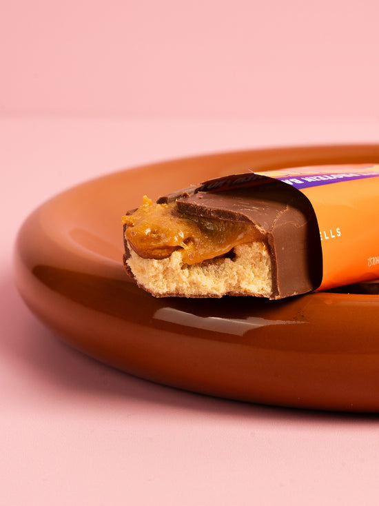 Barebells Salted Peanut Caramel protein bar cut in half showing chocolate coating, peanut caramel filling and cake base on brown plate