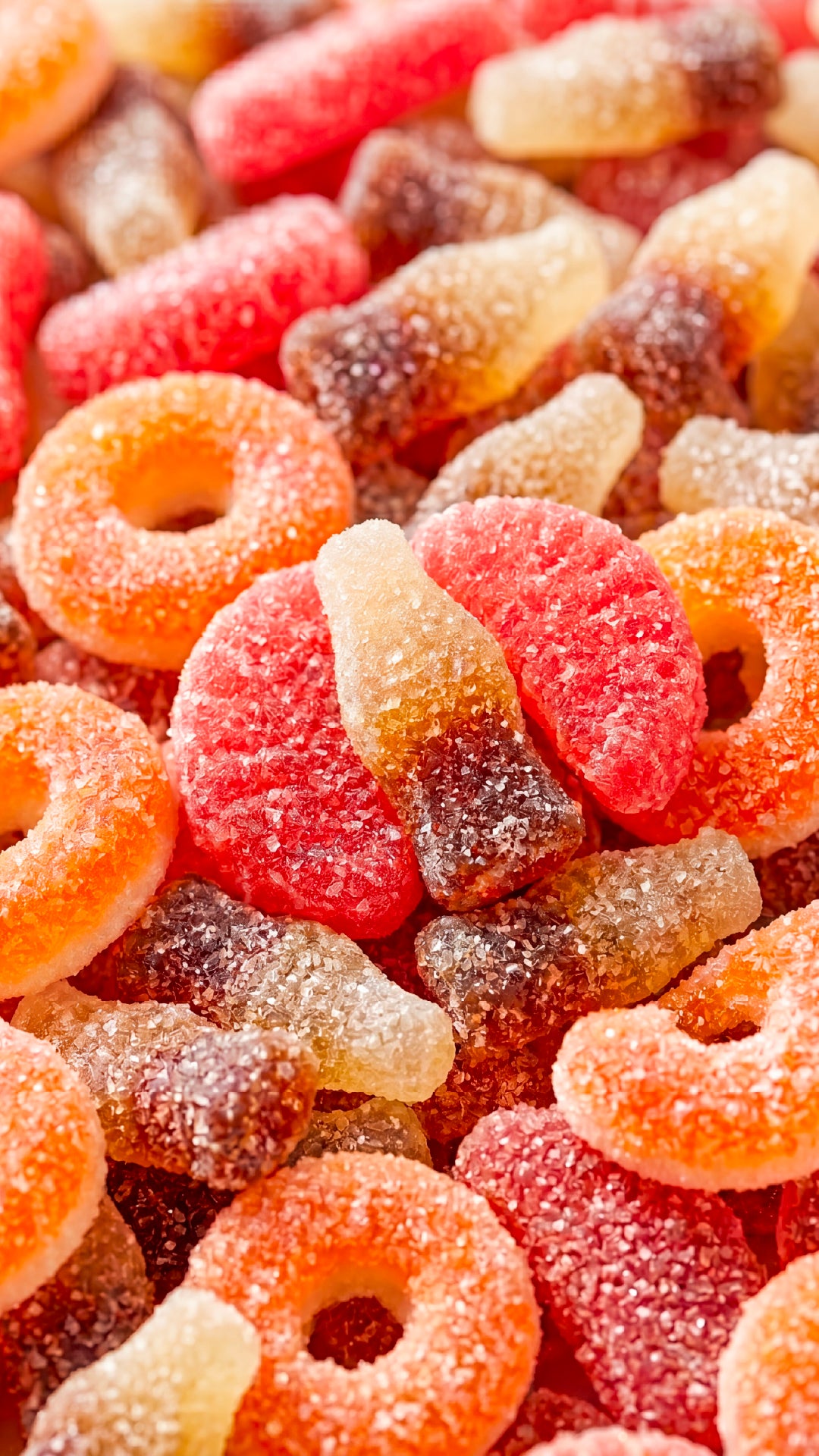 Colorful sugar-coated gummy candies in red, orange, and cream colors with ring and bear shapes